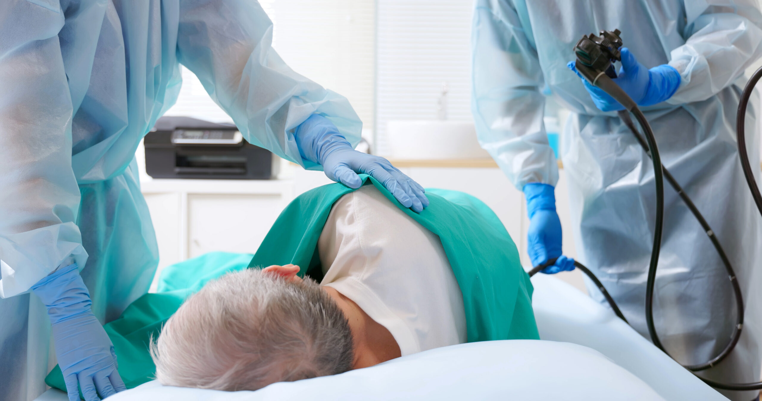 close up asian male doctor wearing protective gown are doing colonoscopy for elderly man while nurse comforting patient in hospital